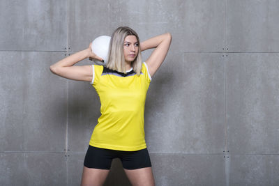 Woman holding sports ball while standing against wall