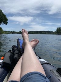 Low section of person relaxing on lake against sky