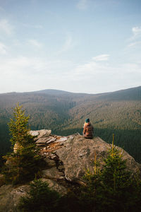 Man sitting on rock looking at mountain against sky