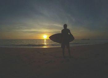 Silhouette man standing on beach against sky during sunset