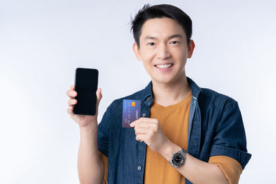 Portrait of smiling man holding camera while standing against white background