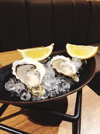High angle view of oysters and lemon slices with ice in container on table