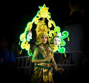 Woman standing by illuminated lighting equipment against black background