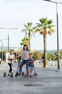 Happy family lifestyle. mother, boy, girl in city. ride scooters. laughing on a summer. fun