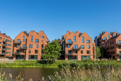 Houses by river and buildings against clear blue sky