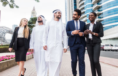 Business people walking on footpath against buildings in city