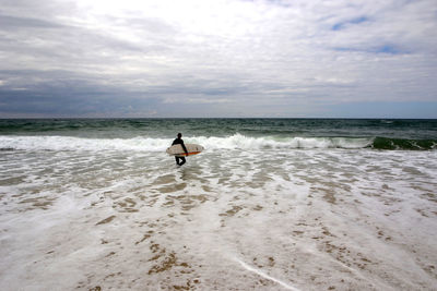 Rear view of surfer in sea against sky