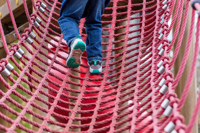 Low section of boy climbing on red rope at playground