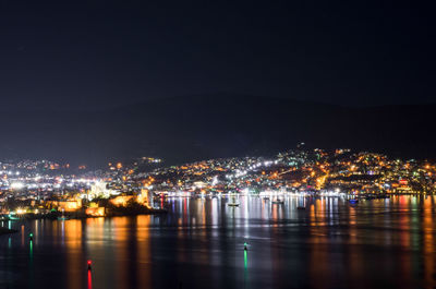 Illuminated city by river against sky at night