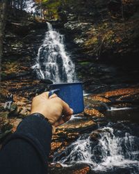 Optical illusion of hand filling cup with waterfall