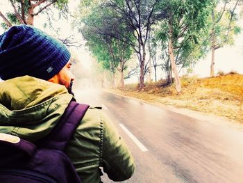 Rear view of man sitting on road by trees