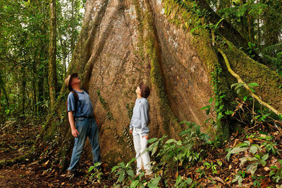 Rear view of friends standing by tree trunk in forest