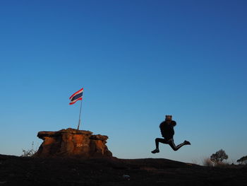 Low angle view of man jumping against clear blue sky