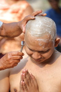 Cropped hand of man cutting hair of monk during ordination