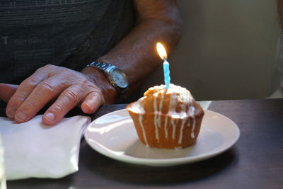 Midsection of man by illuminated candle on cake over table