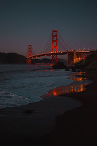 Illuminated bridge over river against sky at night