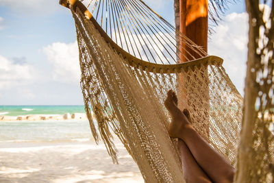 Low section of woman in hammock on beach against sky