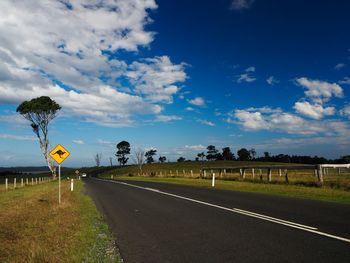 Road passing through field against cloudy sky