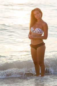 Portrait of confident beautiful woman standing by sea during sunset