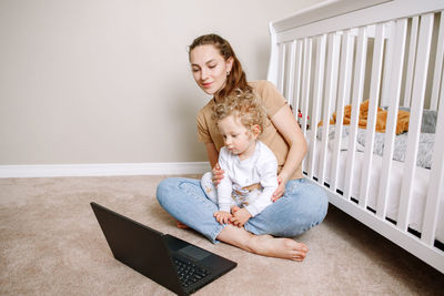 Young caucasian mother with toddler baby boy watching cartoons on laptop at home. 