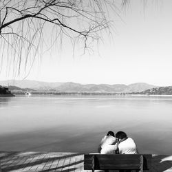 Rear view of man sitting on bench by lake