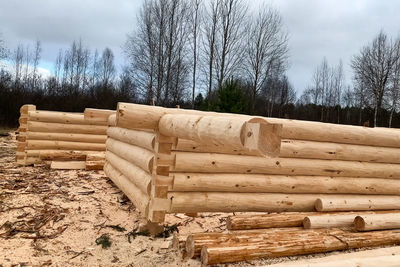 Stack of wooden logs on field against sky