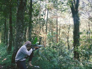 Man aiming rifle while crouching in forest