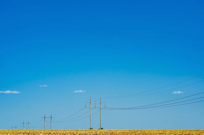 Electrical supports with wires in the field on a background of blue sky