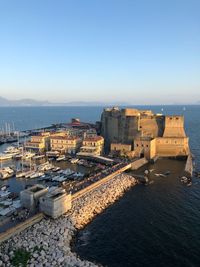 High angle view of buildings and castle by sea against blue sky