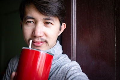 Close-up of smiling young man drinking against wall