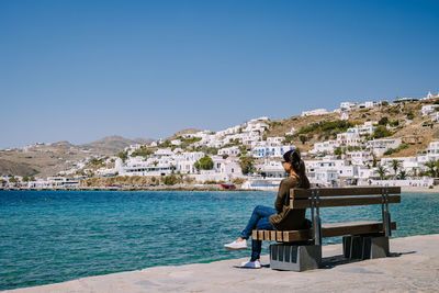 Man sitting on shore against clear blue sky