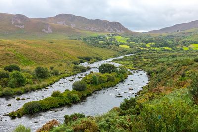 Scenic view of stream by mountains against sky