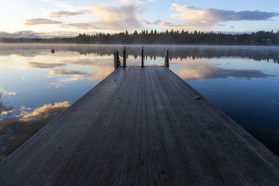 Wooden pier with ladder by lake during sunset and reflection of clouds