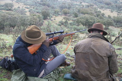 Rear view of men sitting on field with gun