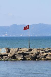 Scenic view of sea by mountain against sky