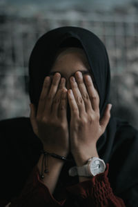 Close-up of woman wearing hijab covering face with hands