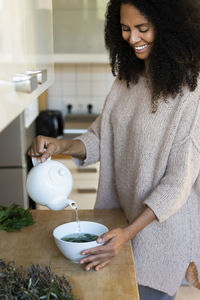 Happy woman pouring water in bowl while to prepare tea at home