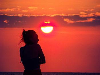 Silhouette woman looking at sea against orange sky