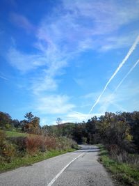 Road amidst trees against blue sky