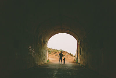 Rear view of father and son walking in tunnel