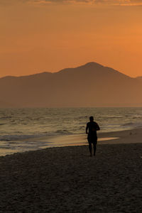 Silhouette man on beach against orange sky