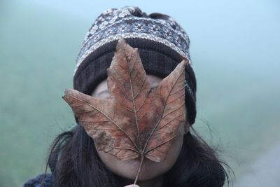 Close-up of woman covering face with dry maple leaf during foggy weather