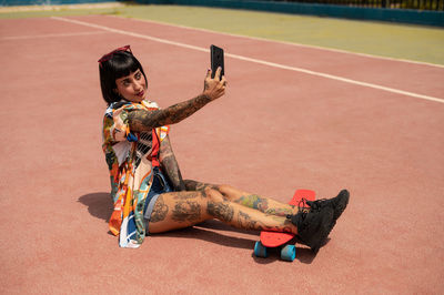 Caucasian girl with tattoos and short black hair on a sports court making a video call
