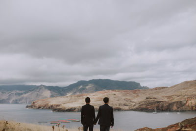 Rear view of men standing on mountain against sky