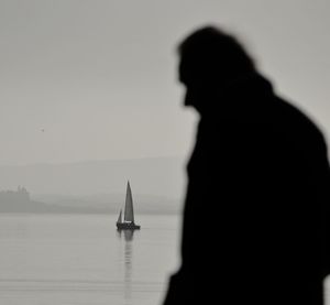 Silhouette people on sailboat by sea against sky