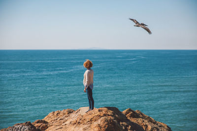 Young woman standing on rock against sea