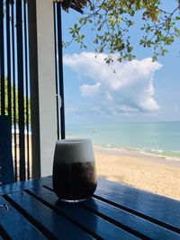 Coffee cup on table by sea against sky