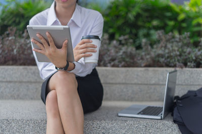 Midsection of businesswoman having drink while using digital tablet outdoors