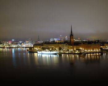 Illuminated buildings by river against sky at night