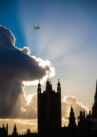 Low angle view of silhouette building against sky during sunset and an airplane flying 